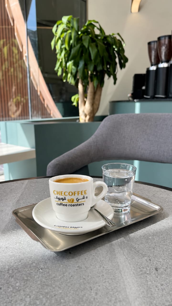 Tasse d'espresso Checoffee servie sur un plateau, avec un verre d'eau